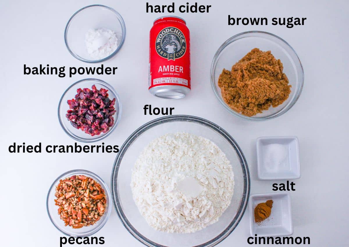 bowls of baking powder, hard cider, brown sugar, flour, dried cranberries, salt, cinnamon and pecans on a white background