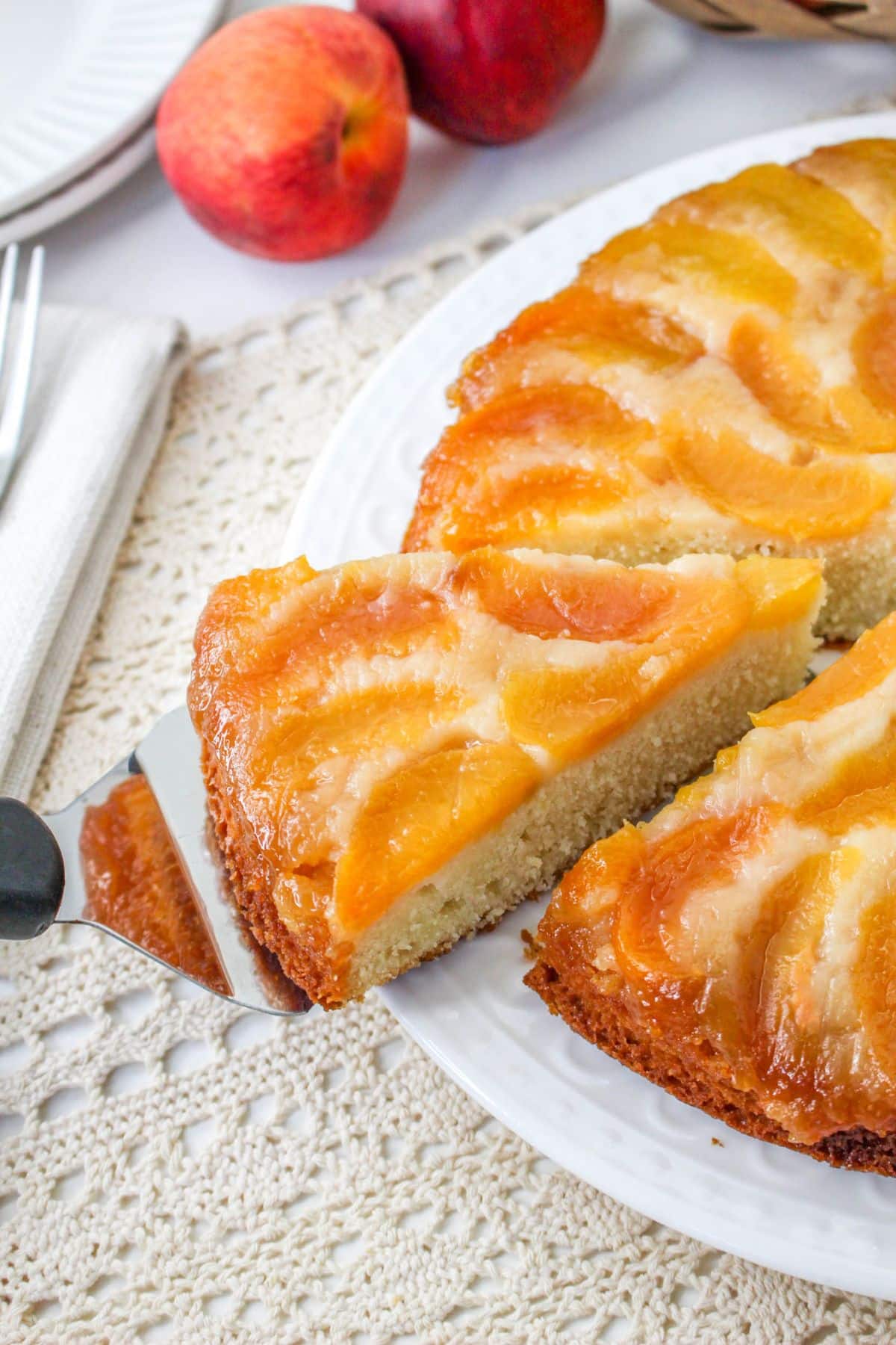 slice of peach upside cake being removed from a white plate with a cake server