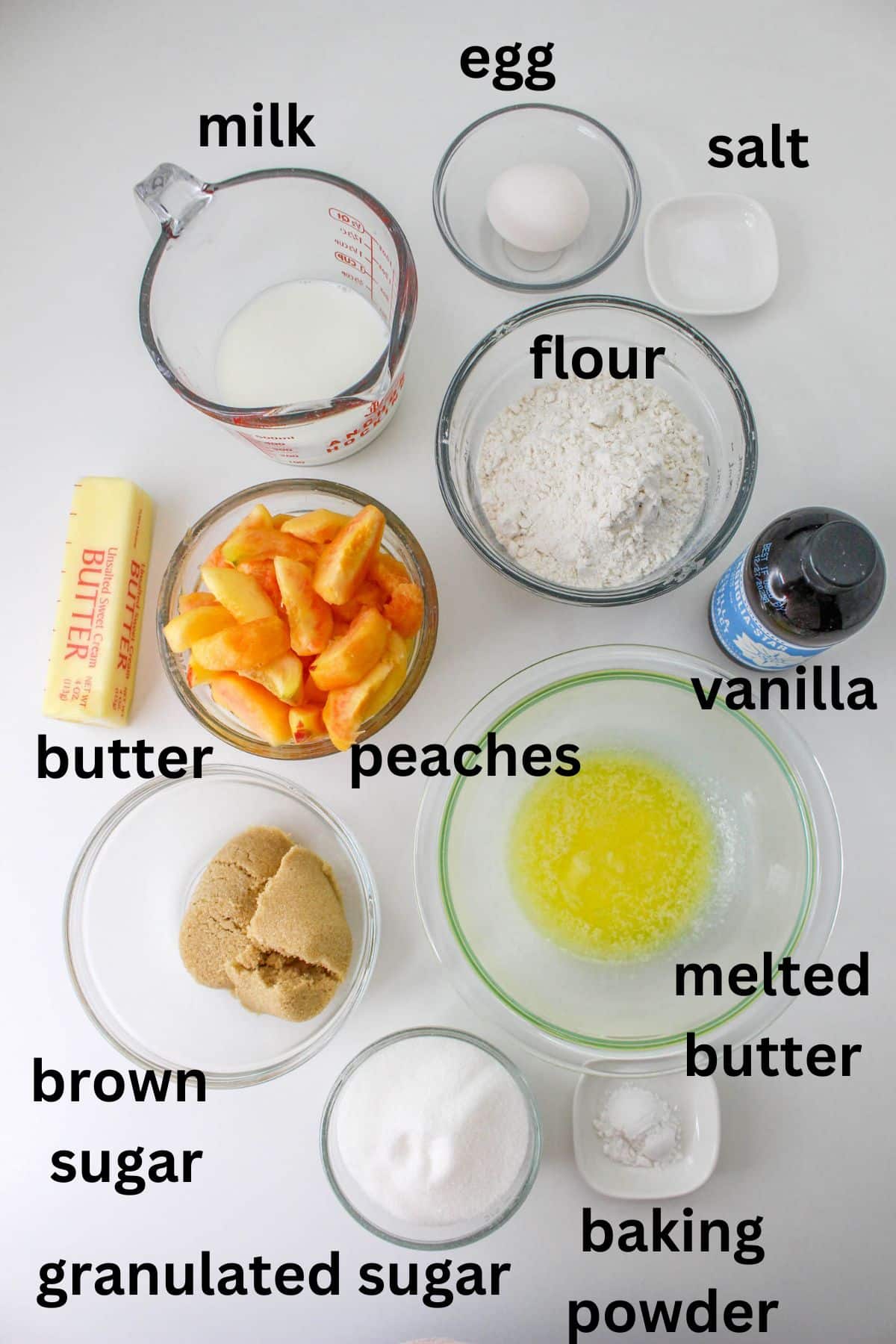 small bowls of salt, egg, milk, peaches, flour, vanilla, brown sugar, butter, granulated sugar, melted butter and baking powder