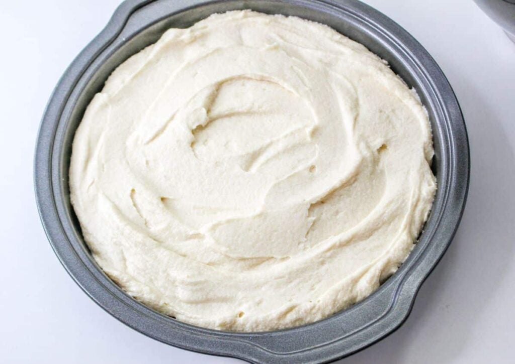 cake batter being spread on top of peaches in a round cake pan