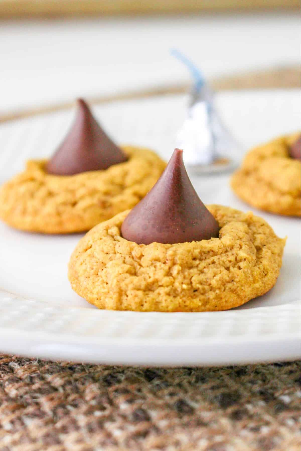three pumpkin blossom cookies on a white plate with a hershey kiss