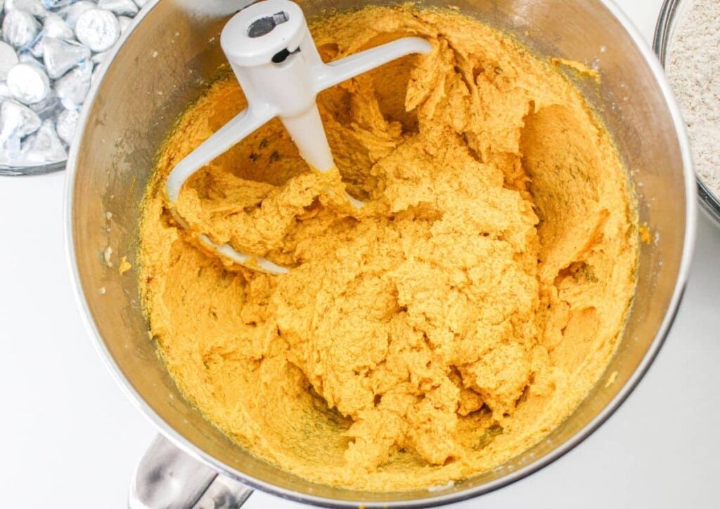 pumpkin and egg added to cookie dough in a stainless steel mixing bowl for a stand mixer