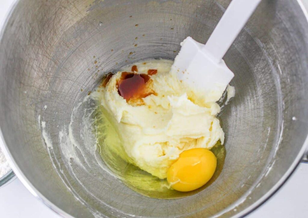 eggs and vanilla being added to butter and sugar in a stand mixing bowl