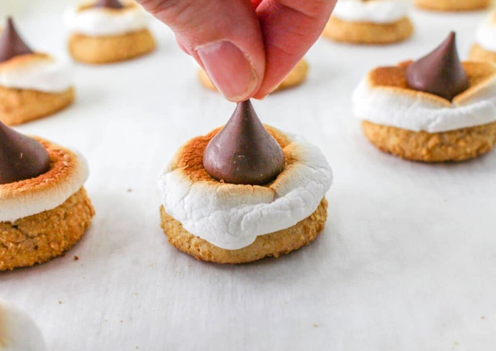 Hershey's Kiss being placed on top of cookies on a parchment lined baking sheet