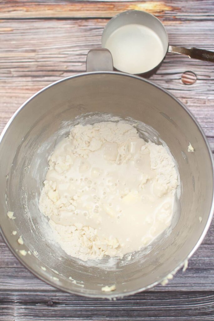 sourdough discard being added to biscuit dough in a stainless steel mixing bowl