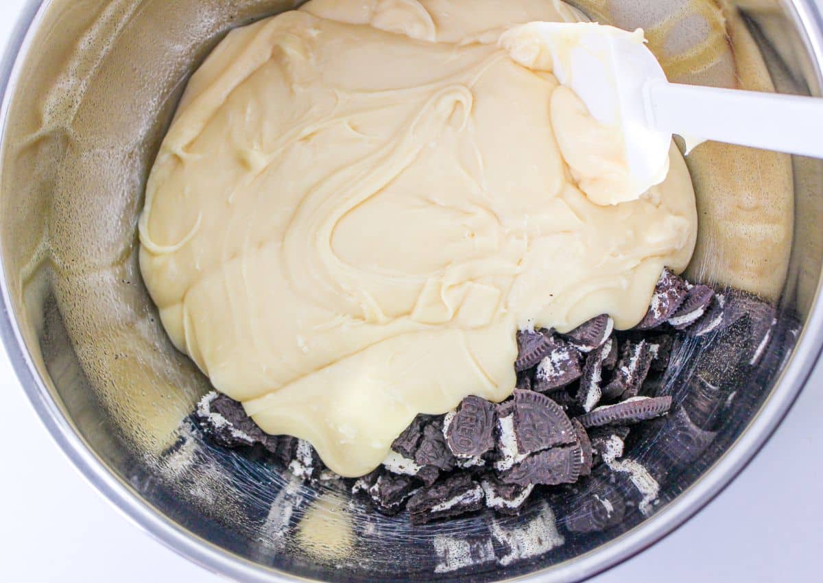 melted white chocolate chips being mixed with chopped Oreo cookies in a stainless steel bowl.
