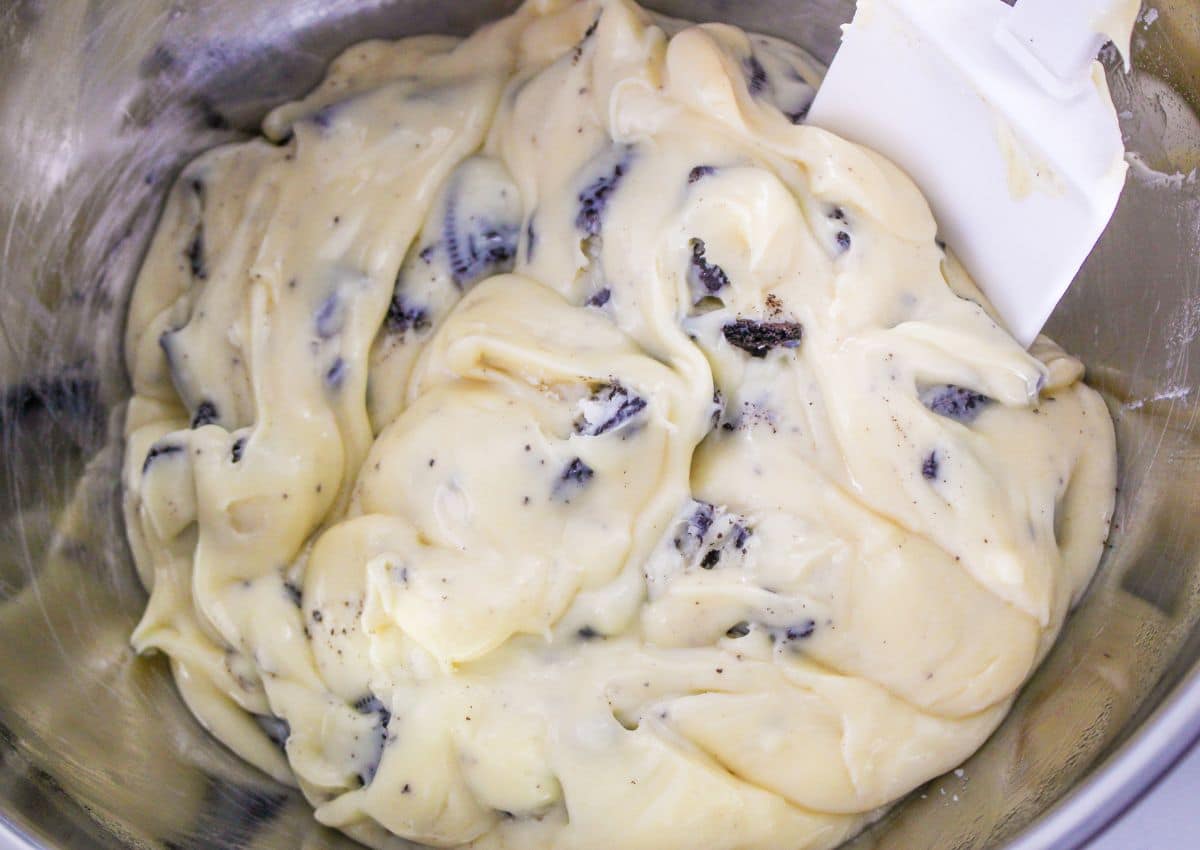 Oreo cookies stirred into the melted white chocolate in a stainless steel mixing bowl.