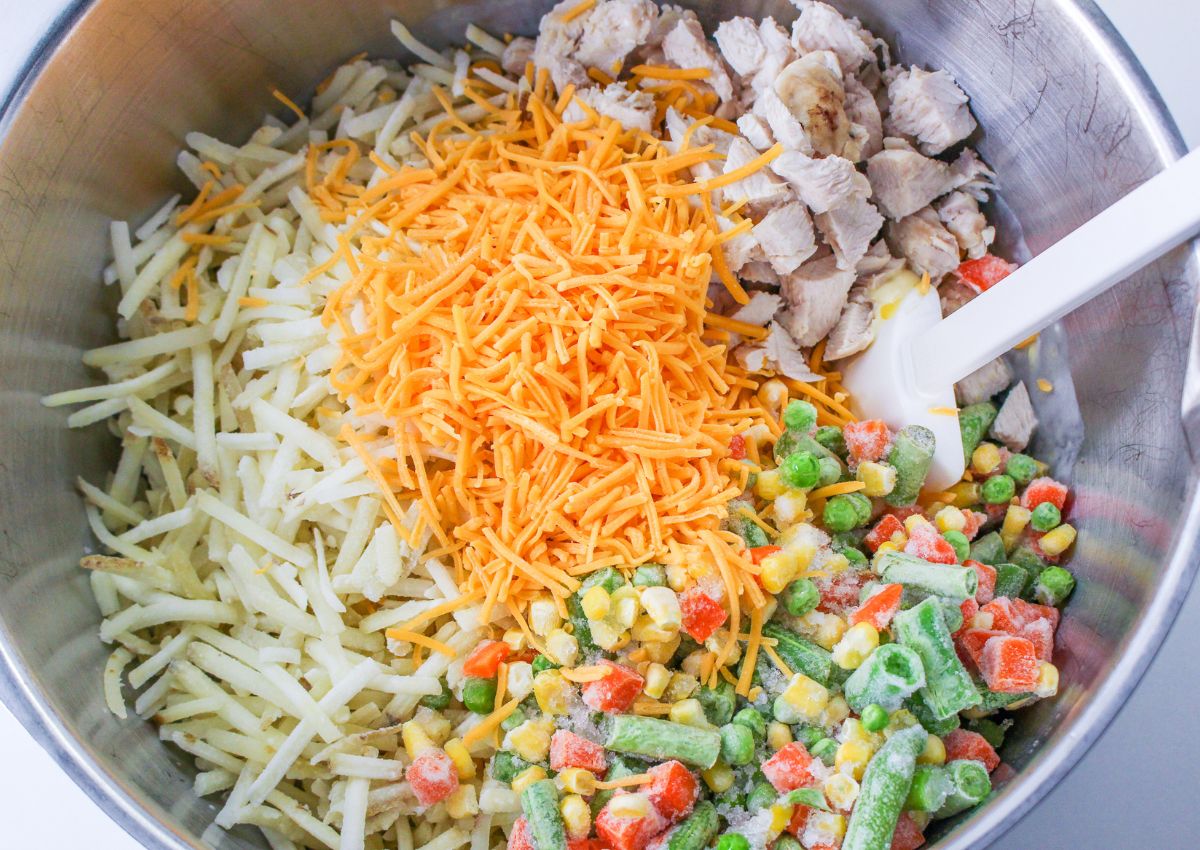 cooked chicken, frozen hashbrowns, cheddar cheese, and frozen mix vegetables being stirred together in a large mixing bowl.