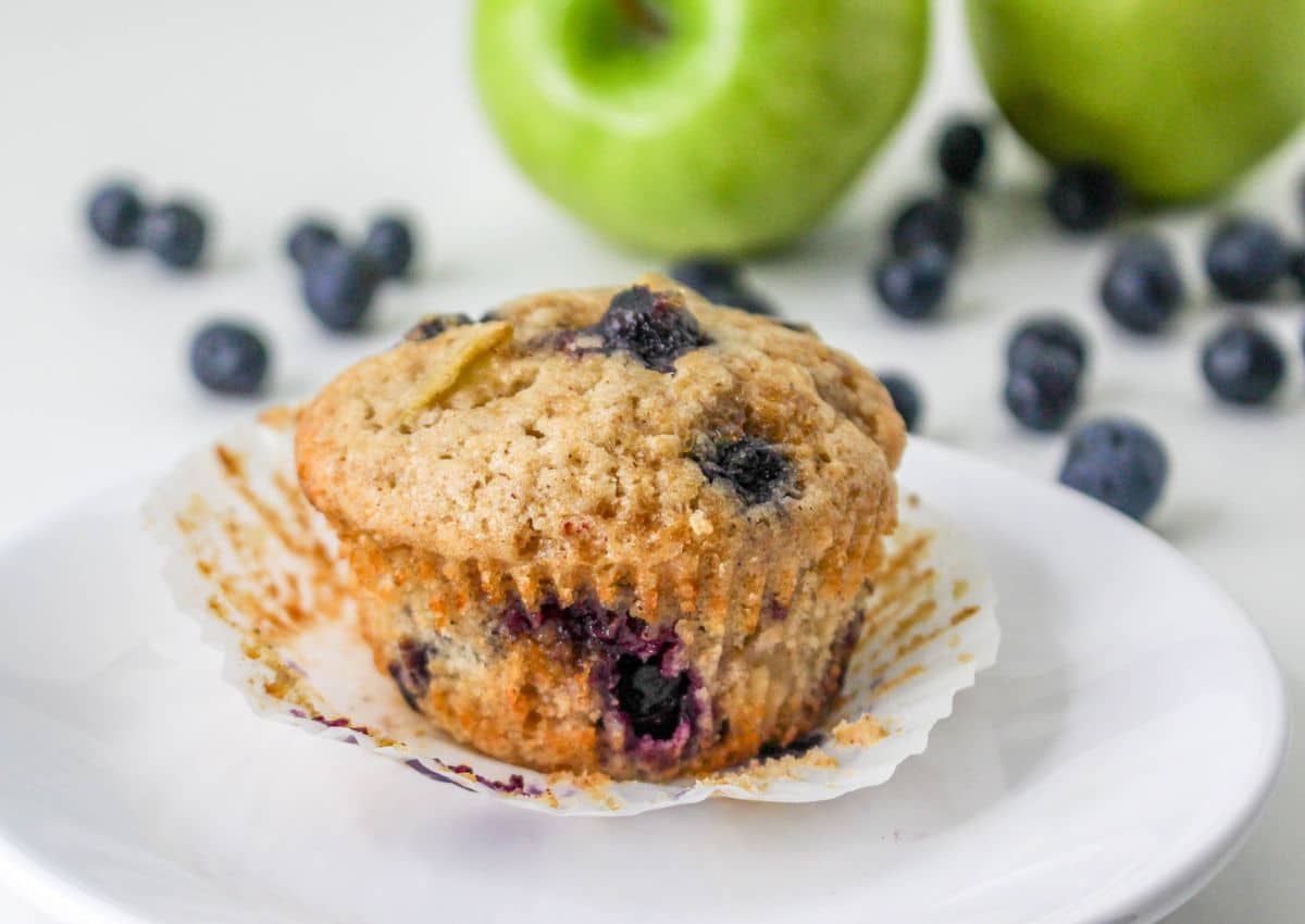 unwrapped apple blueberry muffin on a white plate.