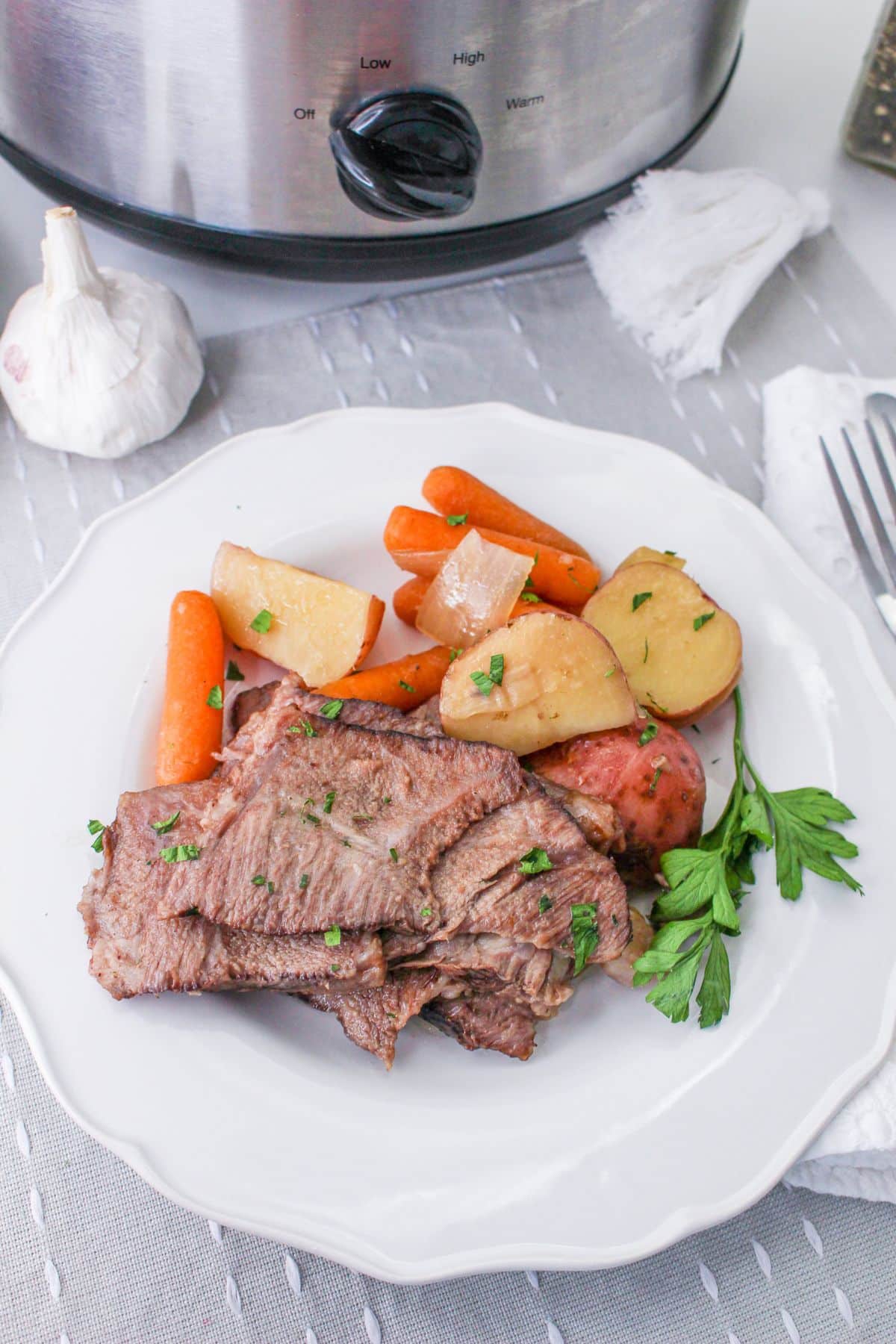 sliced pot roast on a plate with baby carrots, potatoes, and onions.