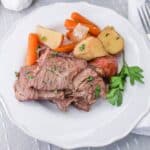 sliced pot roast on a plate with baby carrots, potatoes, and onions.