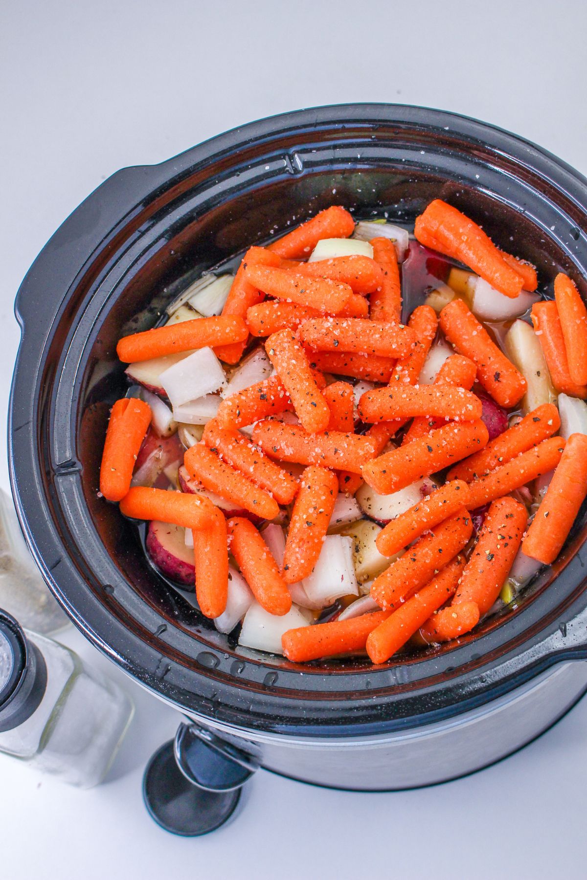 raw carrots, onions, potatoes, and beef roast in a slow cooker.