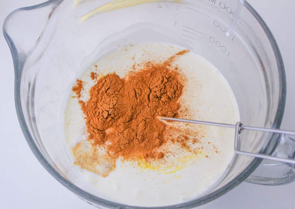 cinnamon, eggs, heavy cream and vanilla being mixed in a large mixing bowl.