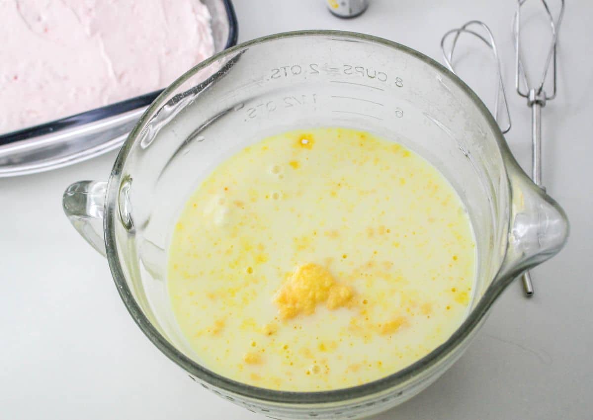 vanilla pudding and milk being mixed in a large measuring cup.