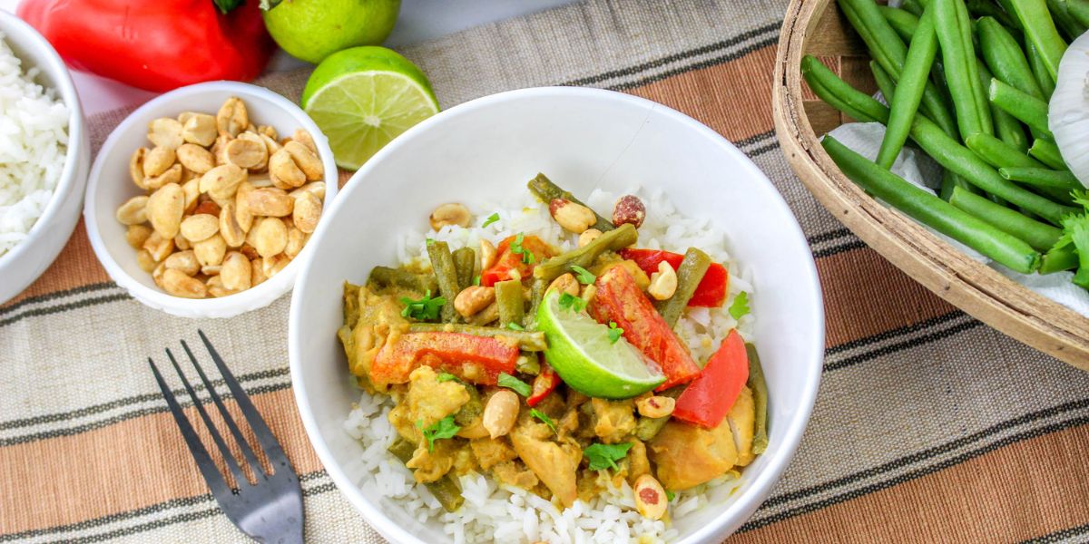 Slow Cooker Chicken Satay in a bowl with rice under and green beans and cashews in bowls around it