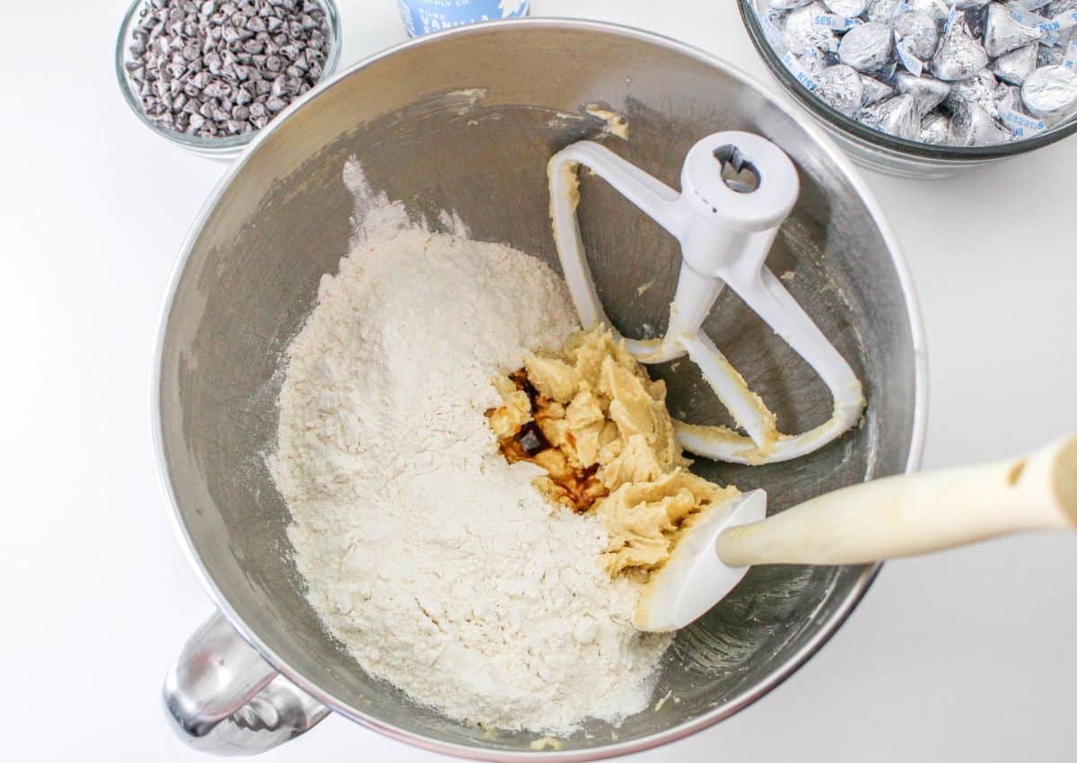 flour and vanilla extract being added to creamed butter and sugar in a stand mixer.