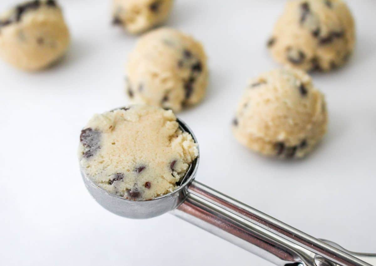 chocolate chip cookie dough being scooped with an ice cream onto a baking sheet.