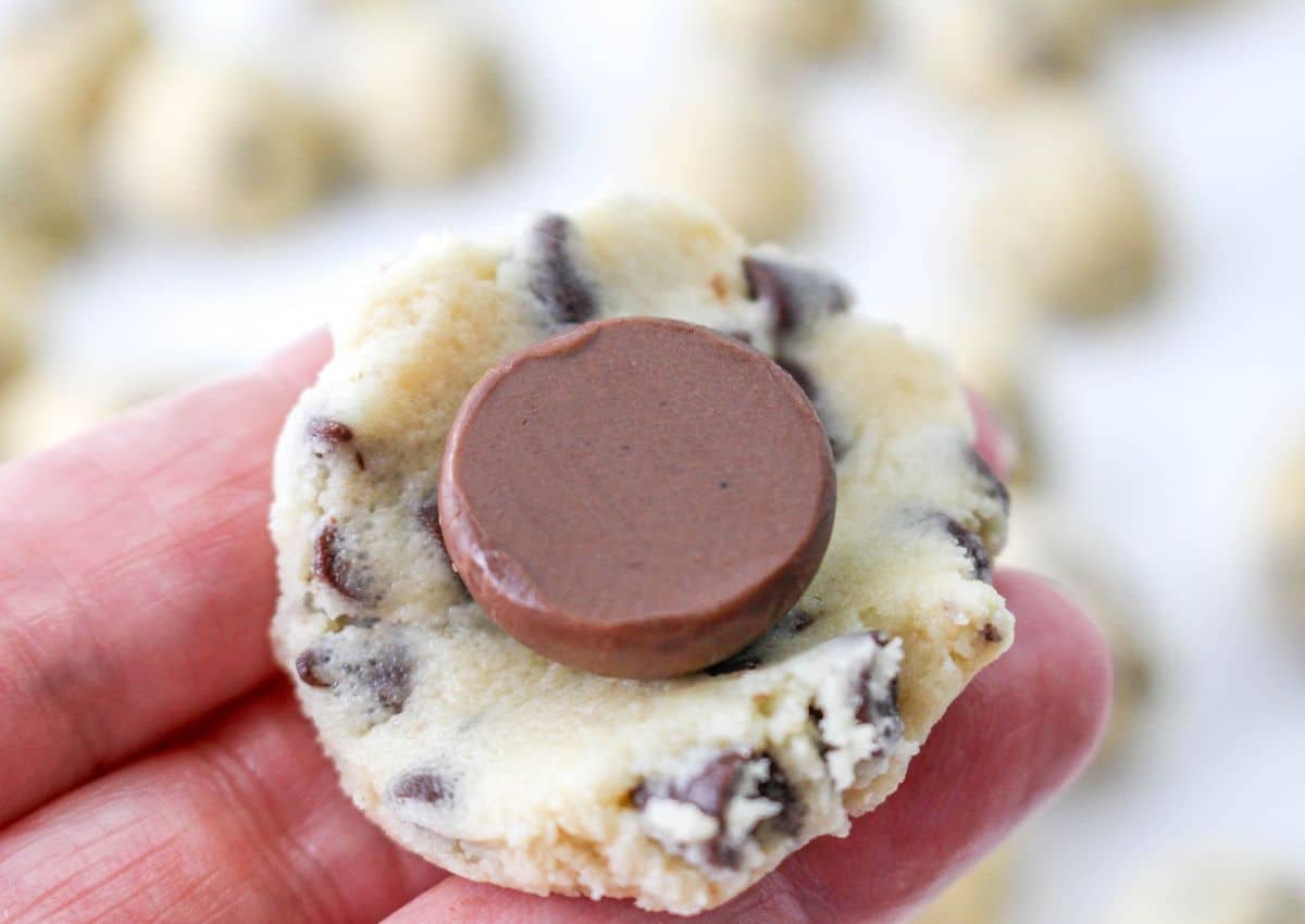 Hershey Kiss being stuffed into the middle of a chocolate chip cookie dough.