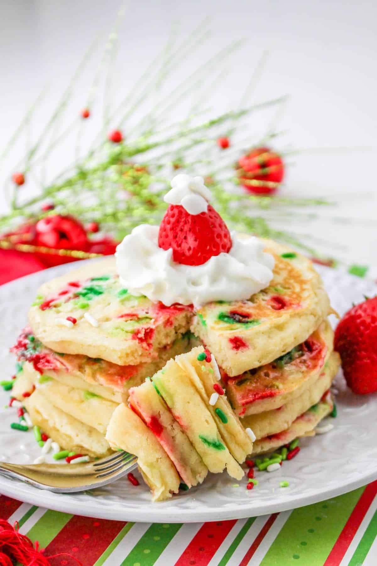 stack of three christmas pancakes on a plate topped with whipped cream and a strawberry.