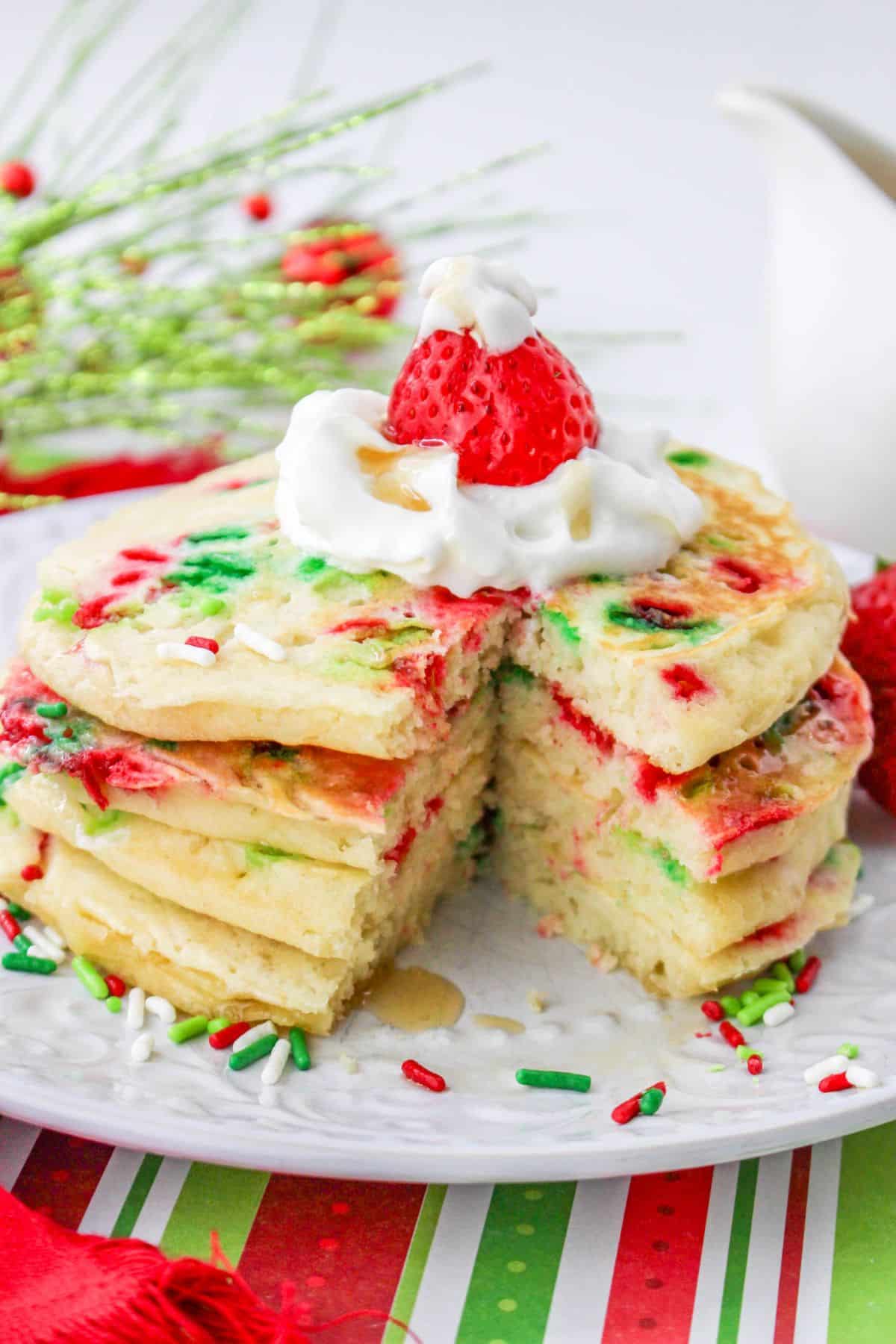 stack of three christmas pancakes on a plate topped with whipped cream and a strawberry.