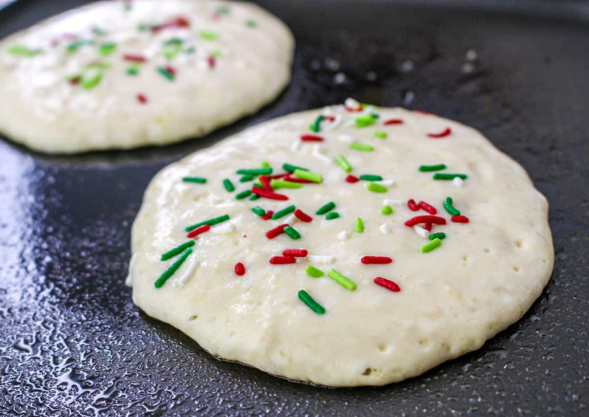 pancakes topped with christmas sprinkles being cooked on a griddle.