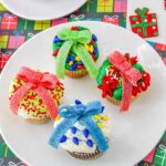 four ugly sweater cupcakes decorated in different colors on a plate.