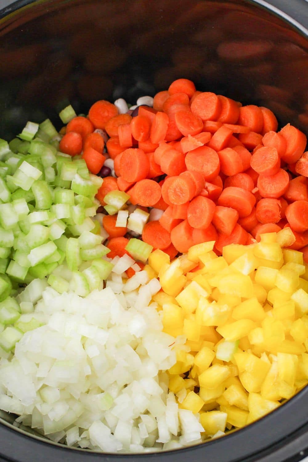 carrots, peppers, celery and onions diced finely topped dried beans in slow cooker on table