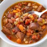 bowl of cajun bean soup with sausage and a spoon on side