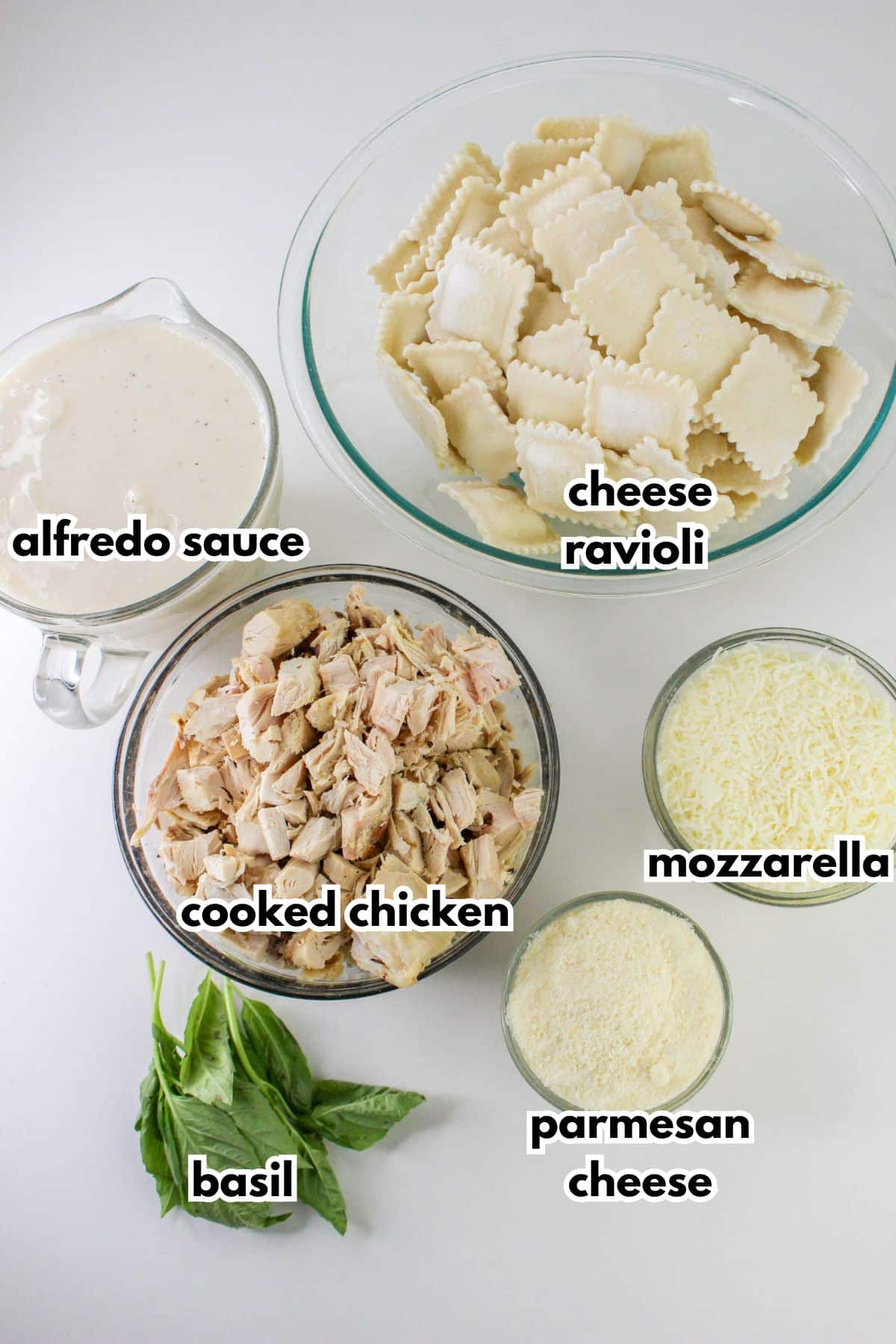 bowls of alfredo sauce, cheese ravioli, cooked chicken, mozzarella cheese, parmesan cheese, and fresh basil.
