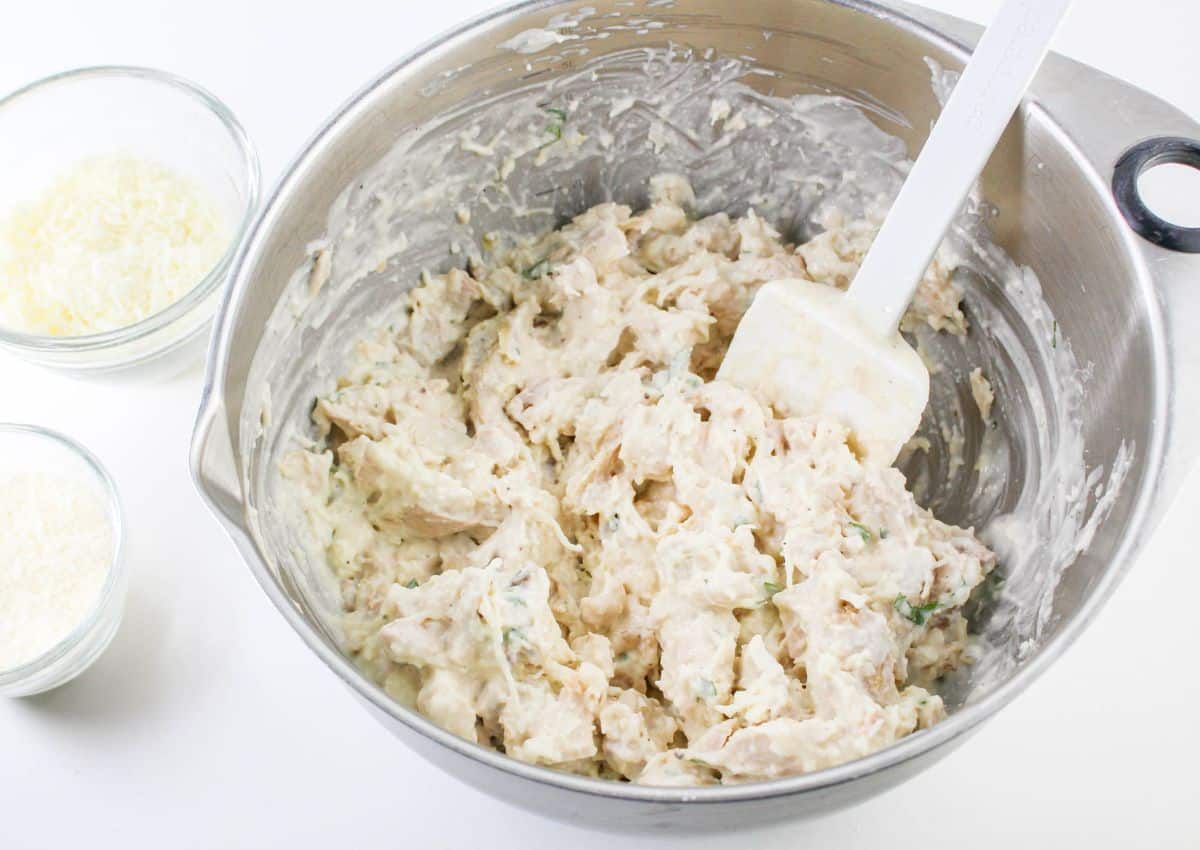 chicken, alfredo sauce, and fresh basil being mixed in a large bowl.