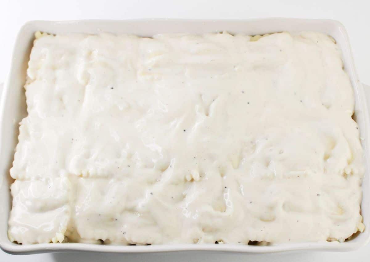 alfredo sauce being spread on top of a casserole dish.