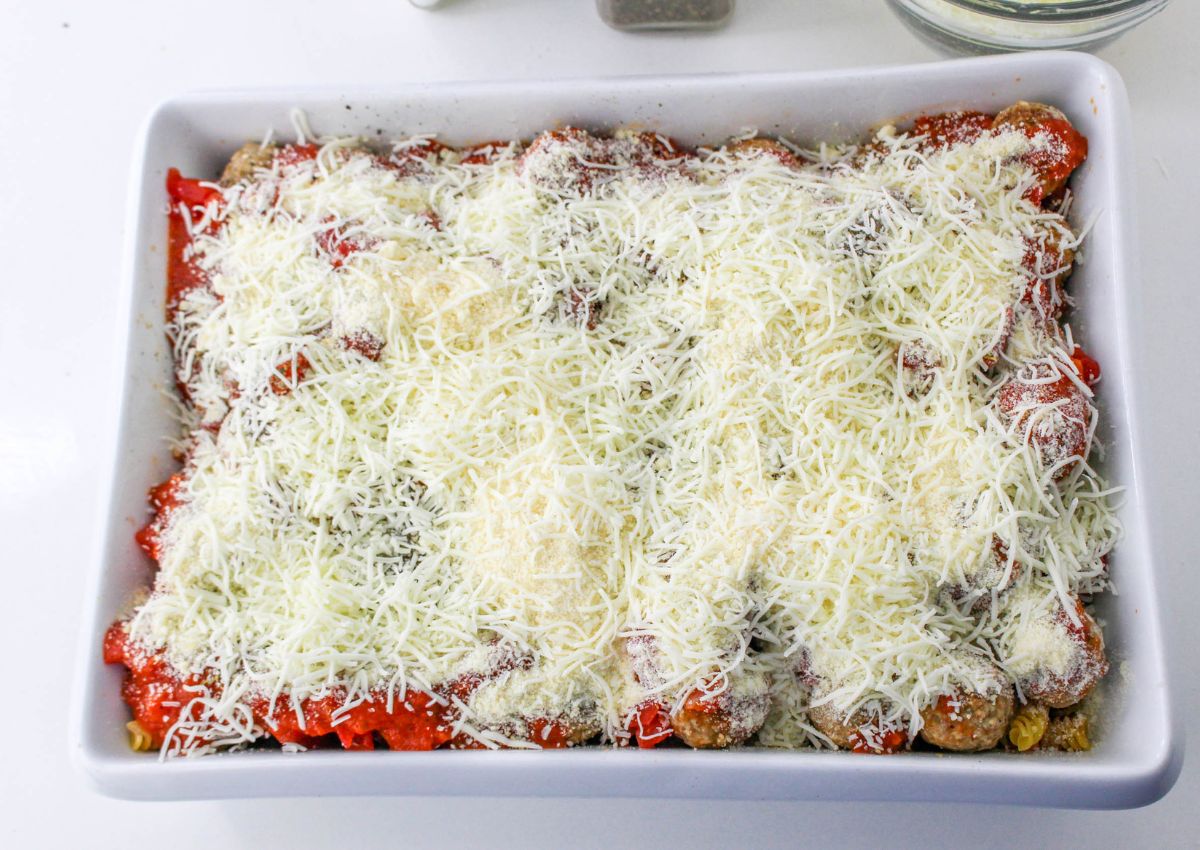 shredded cheese on top of a meatball casserole in a baking dish on the table