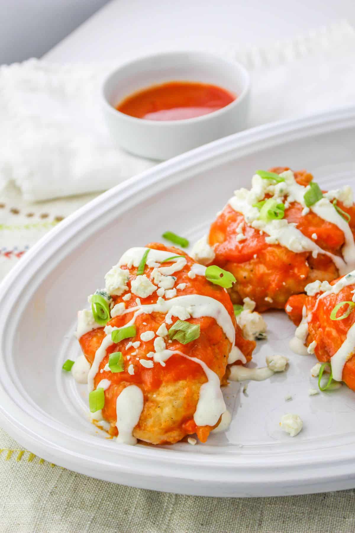 buffalo chicken thighs stopped with ranch dressing and blue cheese crumbles on a plate.