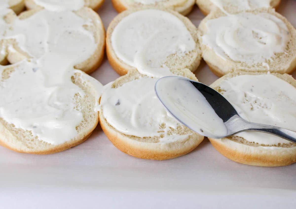 ranch dressing being spread on the bottom of buns.