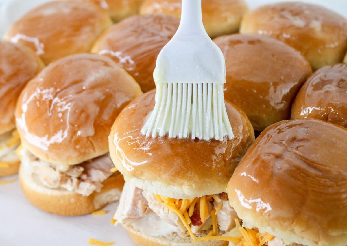 melted butter being brushed on top of sliders.