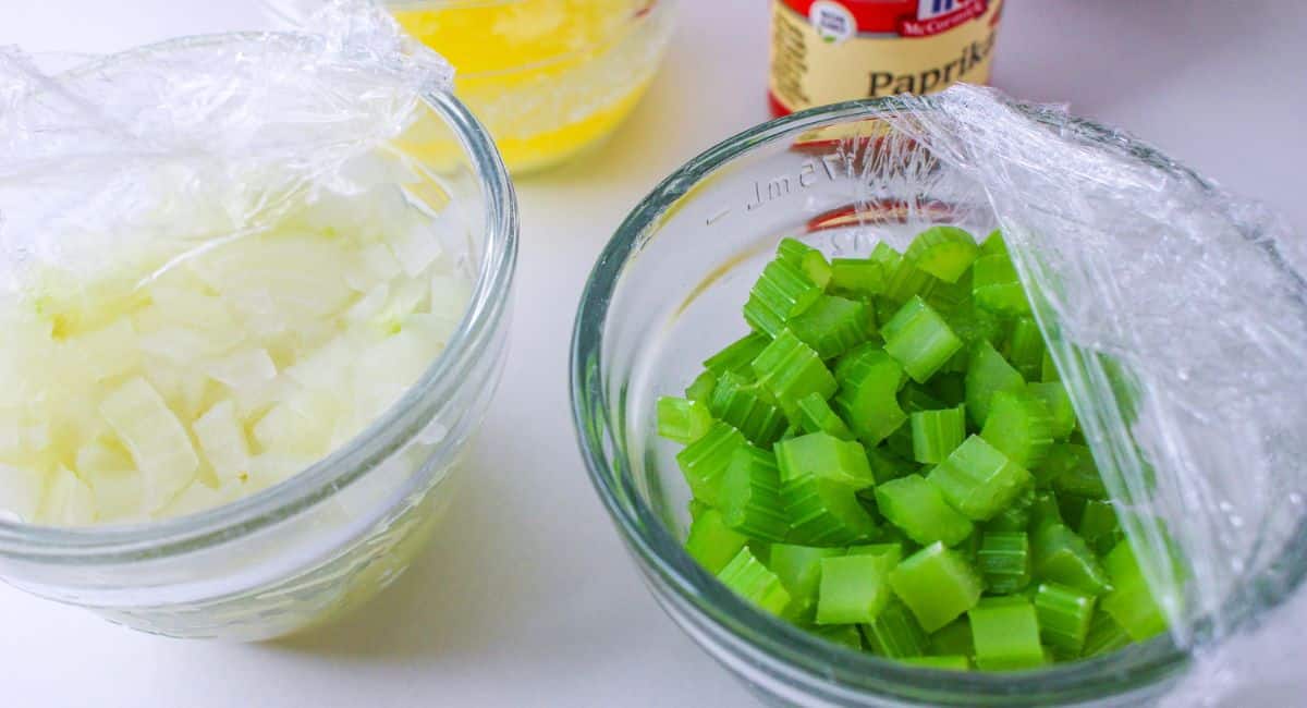 two small bowls filled with celery and onions covered with plastic wrap ready to steam in the microwave.