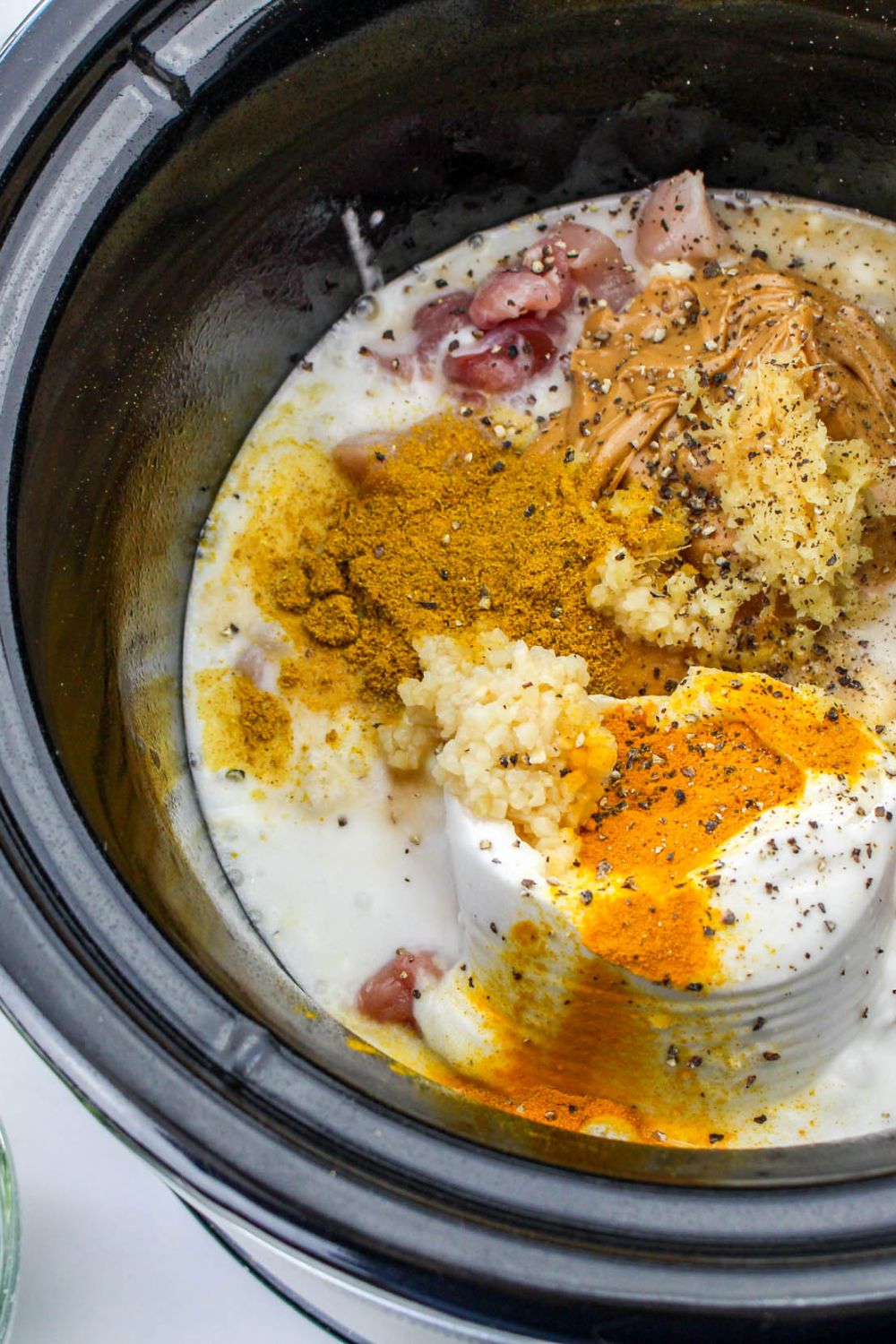 coconut milk, soy sauce, brown sugar, and spices all poured in a slow cooker on top of chicken