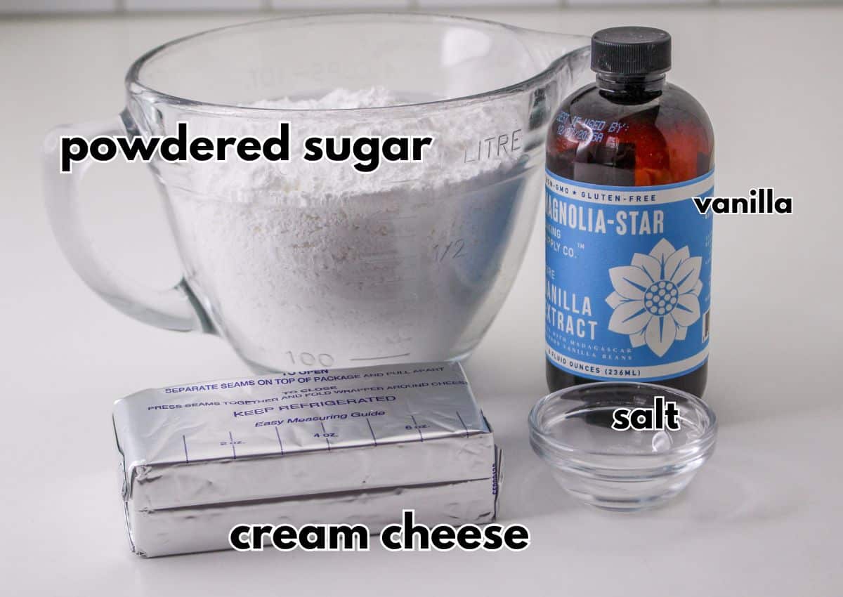 powdered sugar in a measuring cup, bottle of vanilla extract, block of cream cheese and salt in a small bowl on table