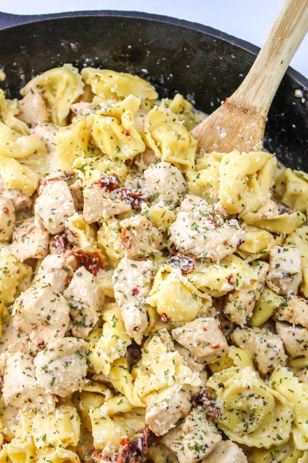 chicken tortellini pasta in a pan on the stove with a wooden spatula on side