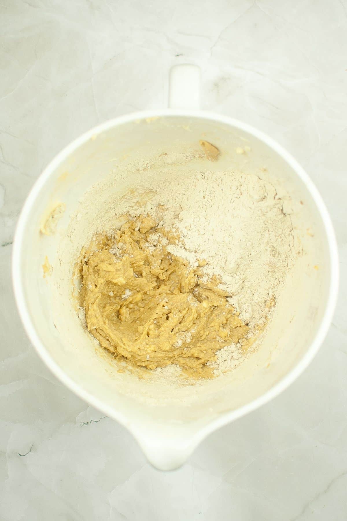 flour being added to creamed butter and sugar in a mixing bowl.