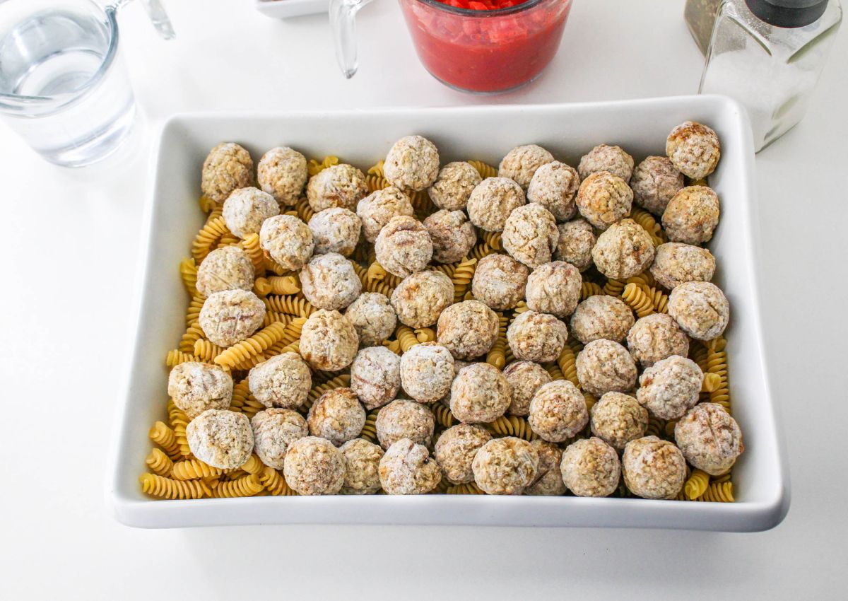 dry pasta and frozen meatballs in a casserole dish on table