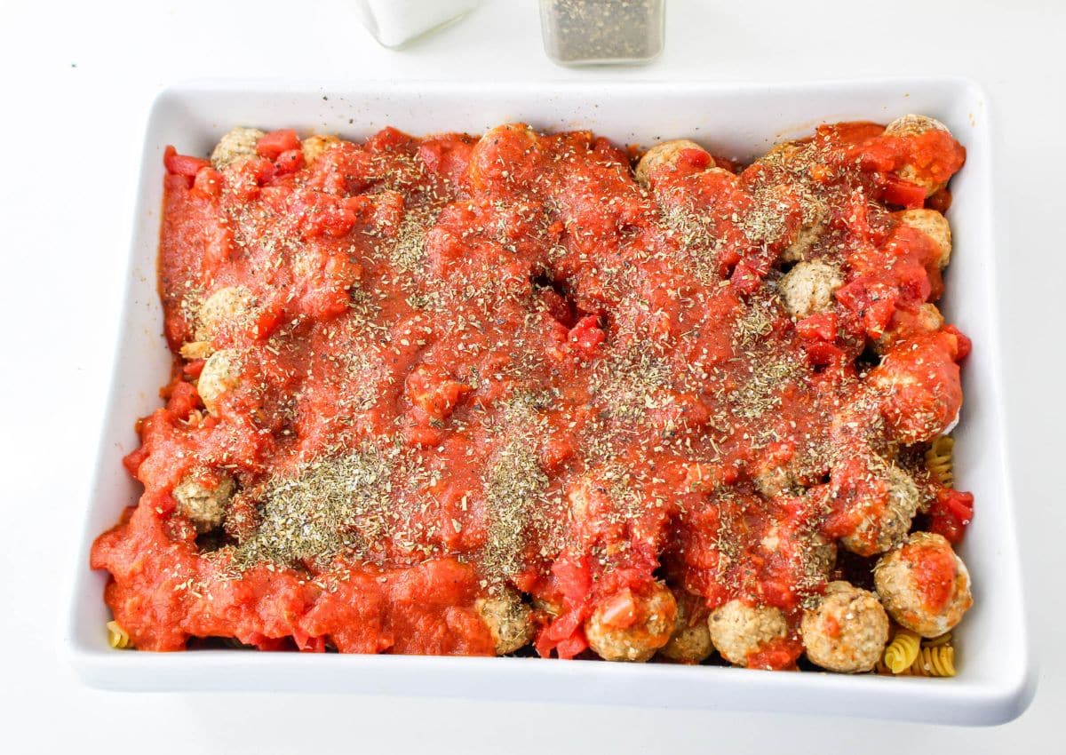 seasonings sprinkled over the top of meatballs in a white casserole dish