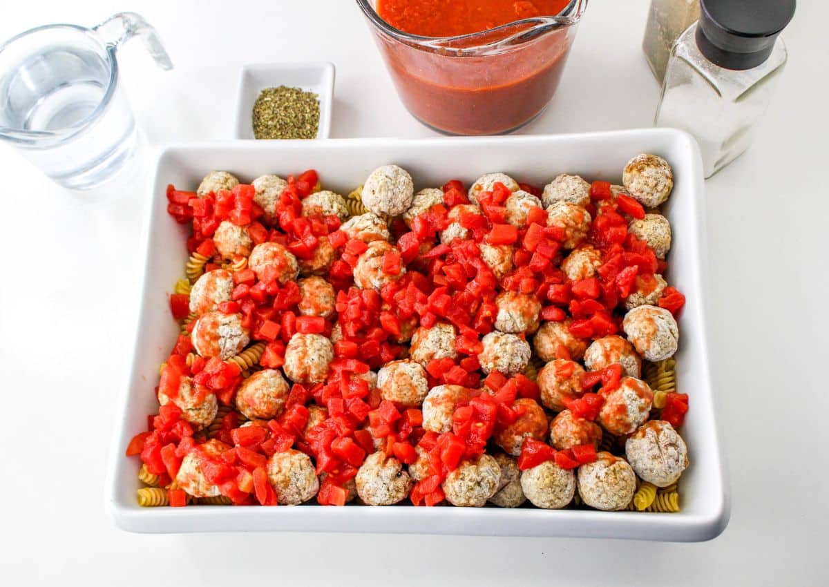 diced tomatoes on top of frozen meatballs in a casserole dish