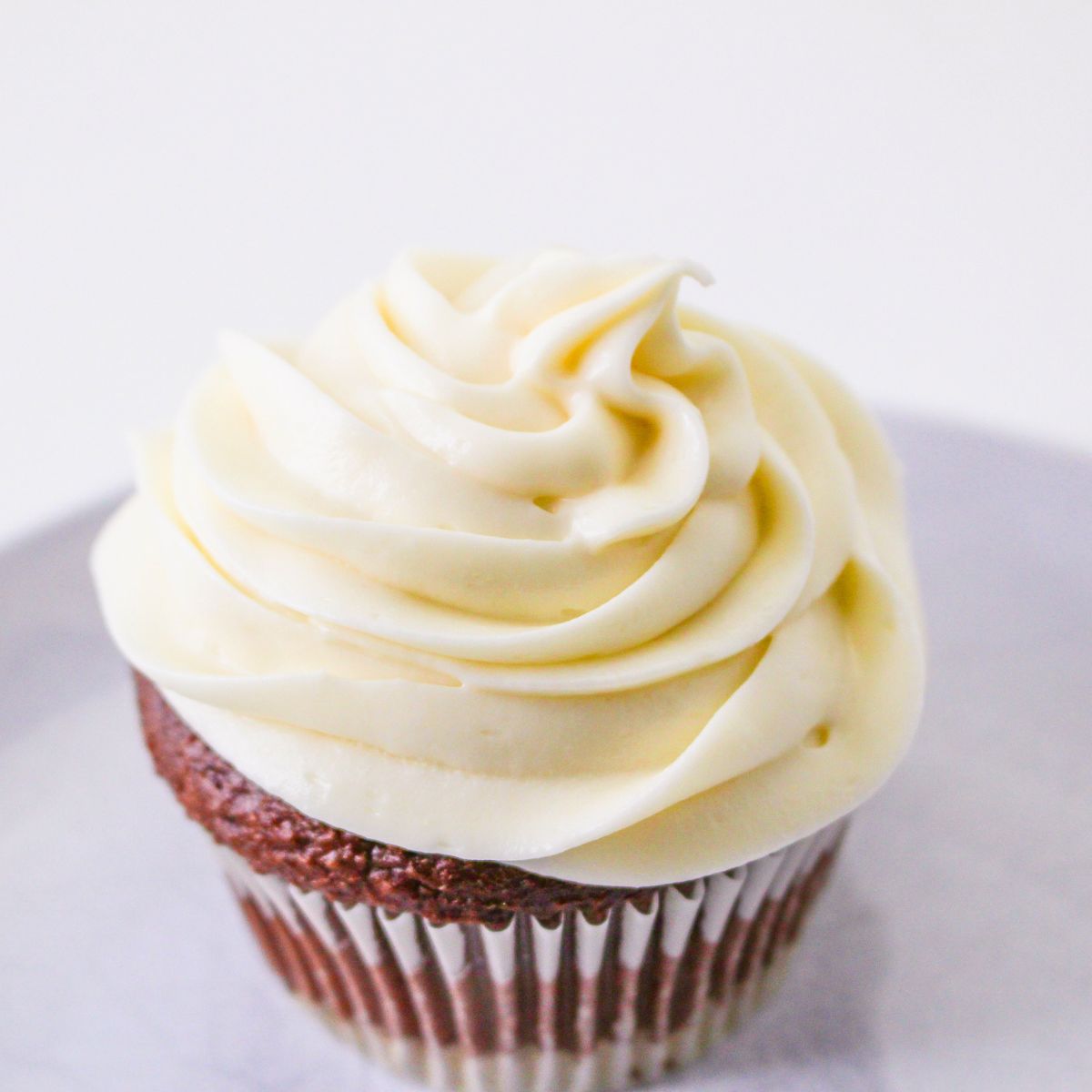 A chocolate cupcake with a swirl of vanilla no butter cream cheese frosting sits on a light-colored surface.