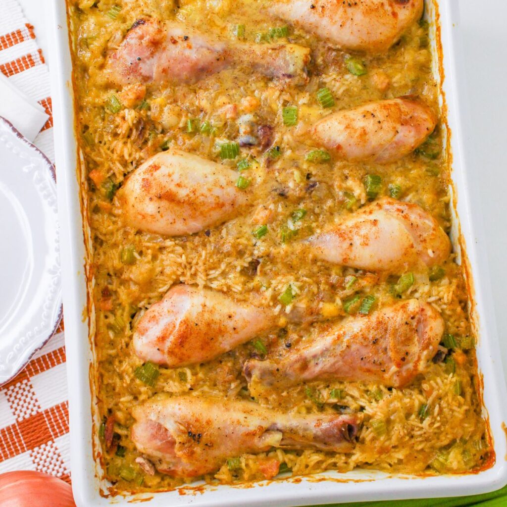 One pan chicken drumsticks and rice, baked to perfection with vegetables, are arranged on top of a casserole in a white rectangular baking dish.