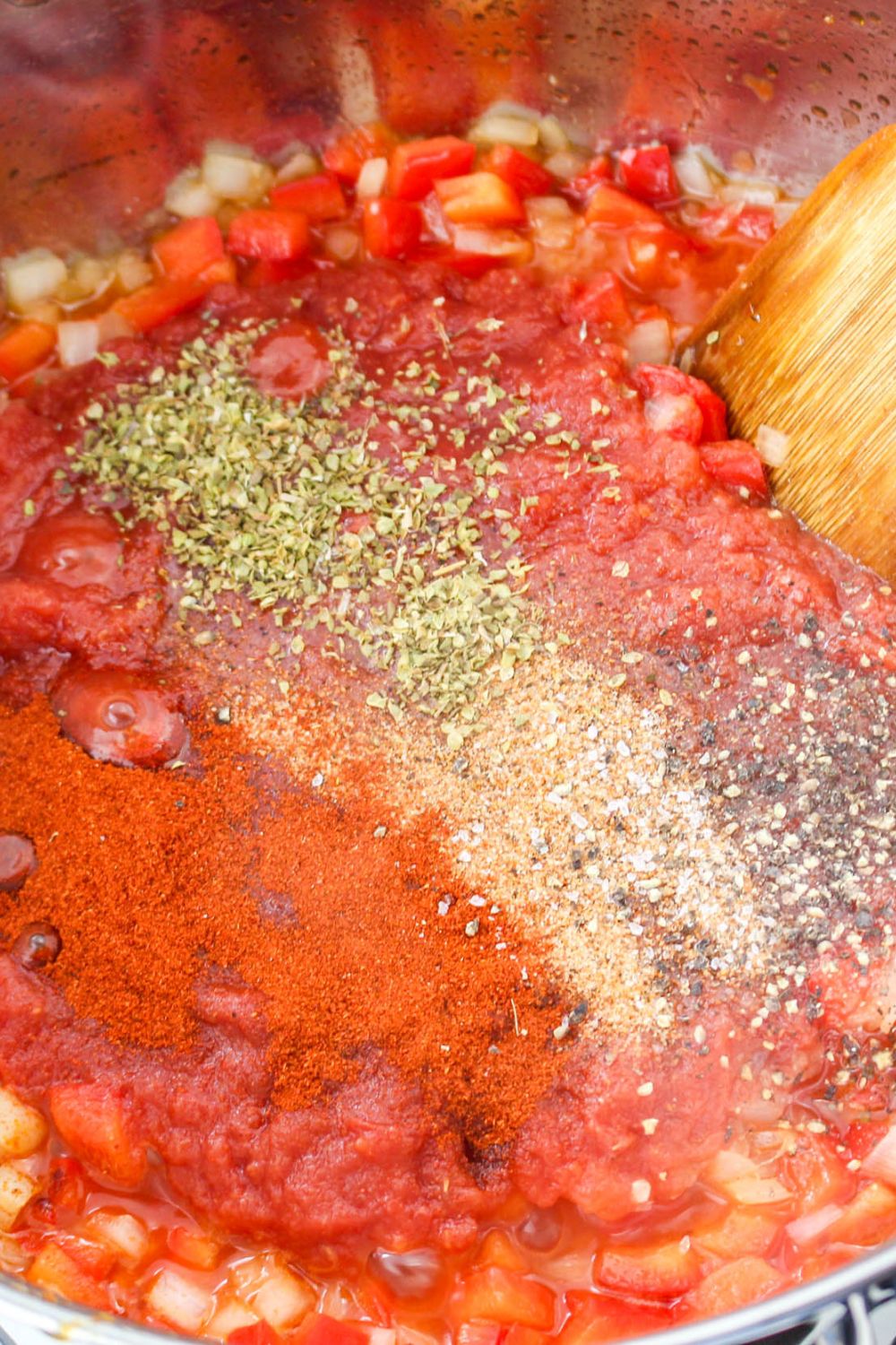 pasta sauce with spices and herbs on top of the tomato sauce base in a skillet on the stove