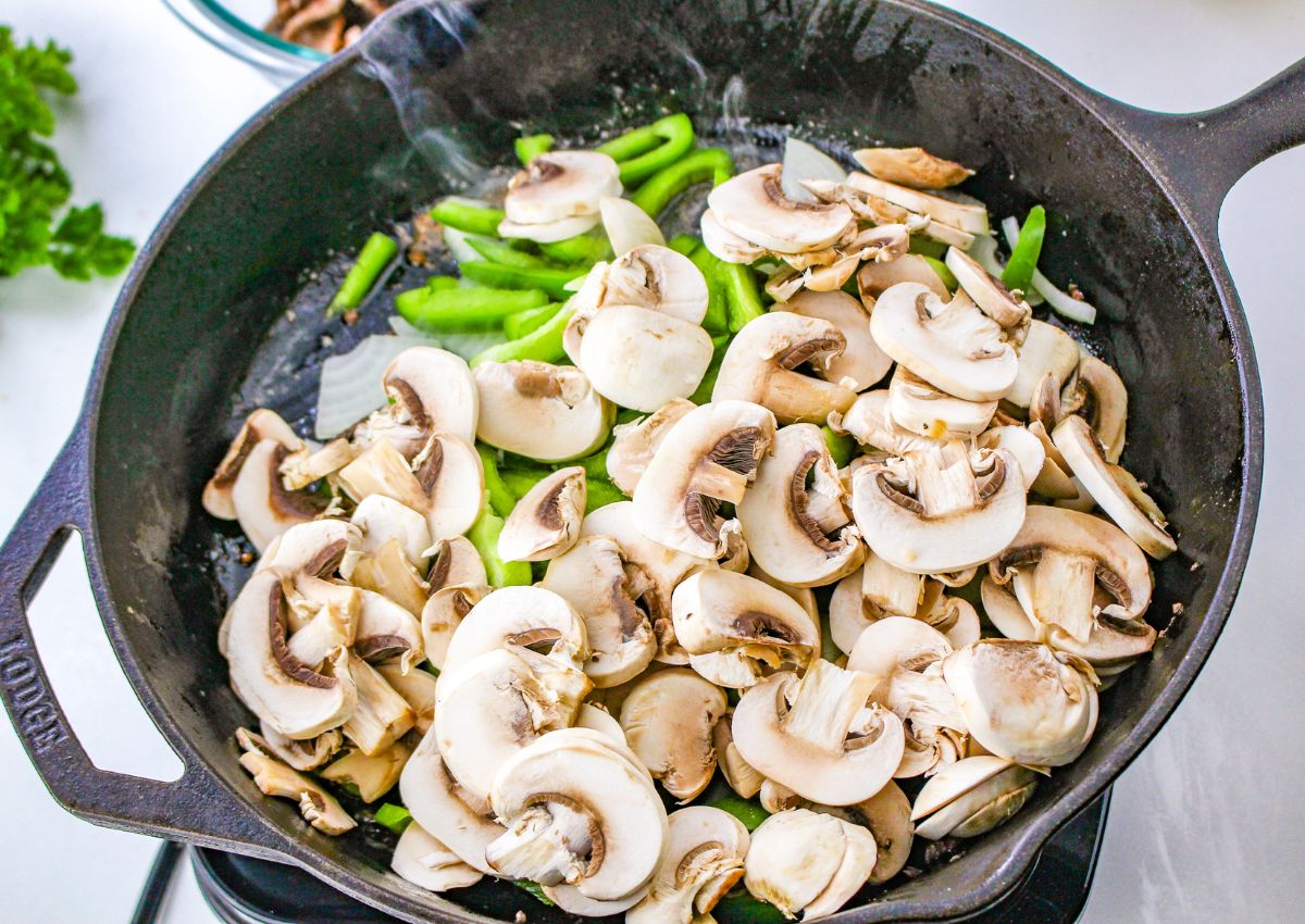 peppers, onions, and mushrooms being cooking in a cast iron skillet.