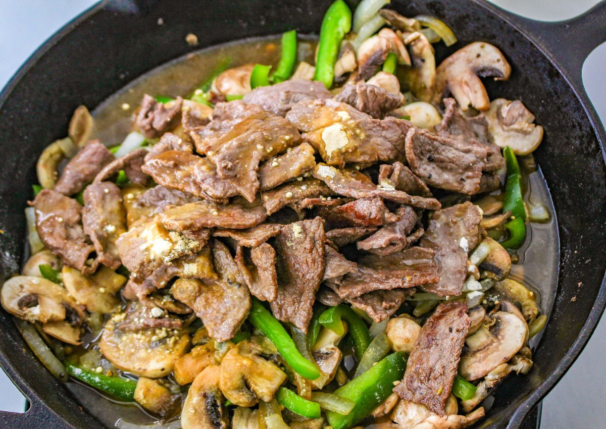 cooked steak, mushroom, onions, and bell peppers in a cast iron skillet.