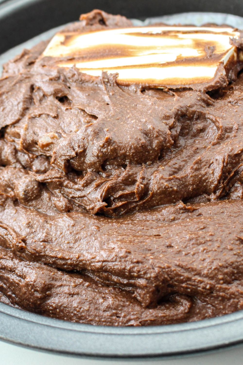 chocolate cake being spread with a spatula in a baking pan
