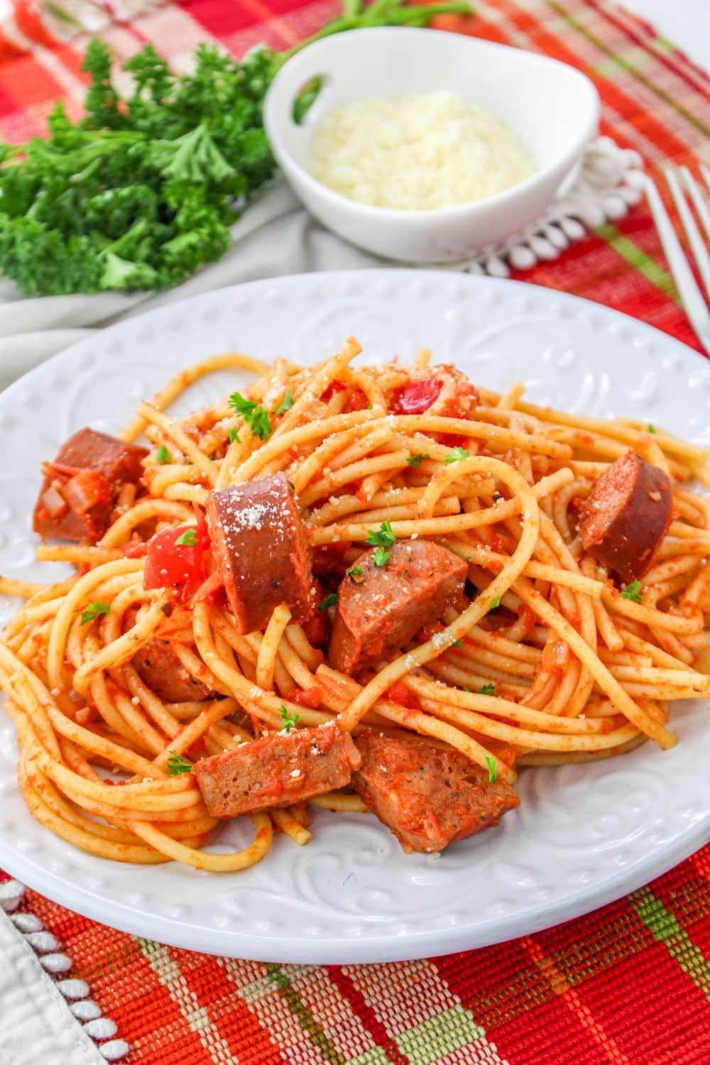 sausage spaghetti piled on plate with parsley and a bowl of parmesan sitting behind it on table